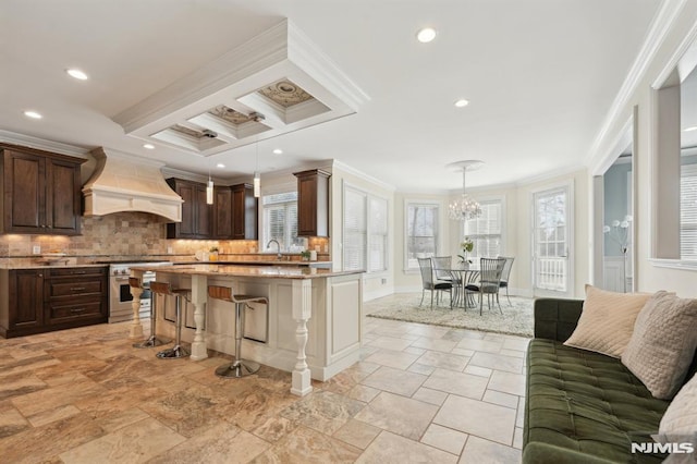 kitchen with high end stainless steel range, ornamental molding, dark brown cabinets, premium range hood, and a kitchen bar