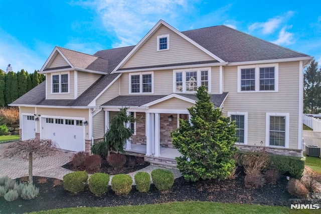 view of front of home with a porch, a garage, central AC, stone siding, and roof with shingles