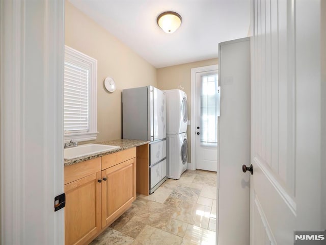 kitchen with stacked washer and clothes dryer, light countertops, a sink, and light brown cabinetry