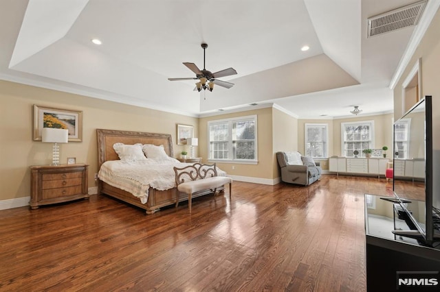 bedroom featuring a tray ceiling, multiple windows, wood finished floors, and visible vents