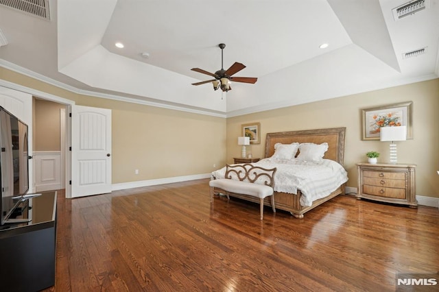 bedroom with a tray ceiling, visible vents, baseboards, and wood finished floors