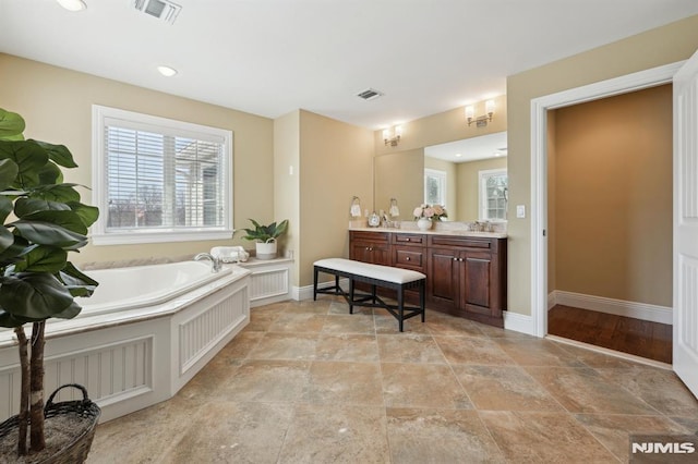 bathroom with vanity, a garden tub, visible vents, and baseboards