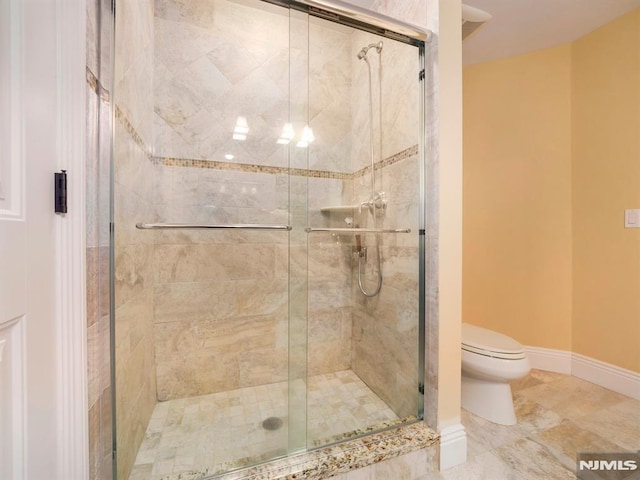 bathroom featuring toilet, a shower stall, and baseboards