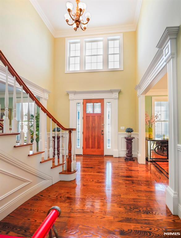 foyer featuring a wainscoted wall, wood finished floors, stairs, crown molding, and a notable chandelier