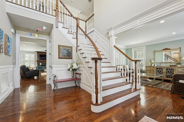 stairs with a decorative wall, wainscoting, wood finished floors, and crown molding