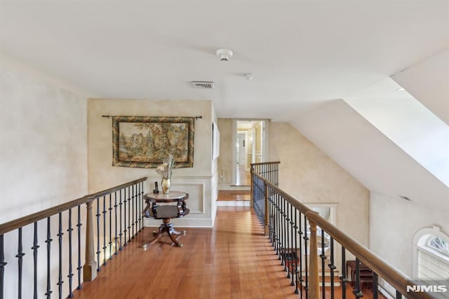 corridor featuring visible vents, wood finished floors, an upstairs landing, and lofted ceiling