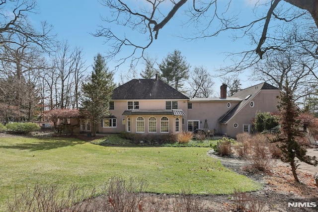 rear view of house featuring a lawn, a chimney, and stucco siding