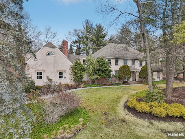 view of front of property featuring a chimney, a front lawn, and stucco siding