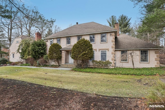 view of front of property featuring a front lawn, a chimney, a shingled roof, and stucco siding