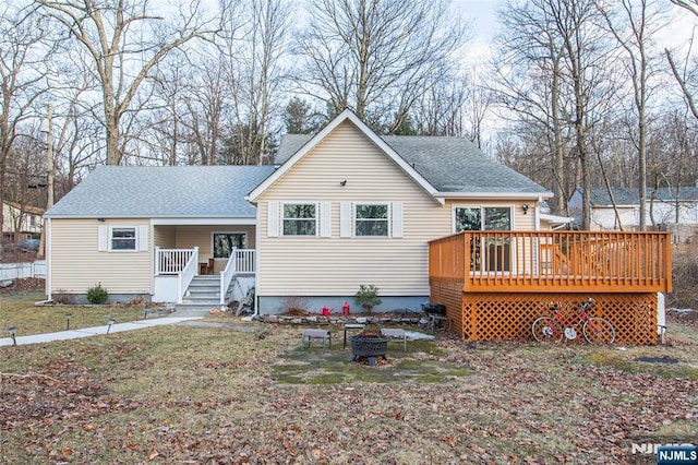 view of front of home featuring an outdoor fire pit, a front lawn, a shingled roof, and a wooden deck