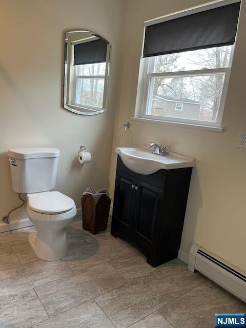 half bathroom with toilet, a baseboard radiator, vanity, and a wealth of natural light