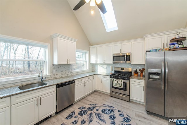 kitchen with a sink, light wood-style floors, white cabinets, appliances with stainless steel finishes, and backsplash