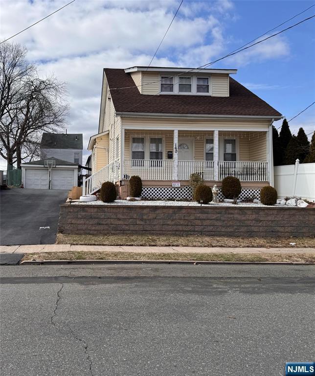 bungalow-style house with a garage, roof with shingles, an outbuilding, covered porch, and fence