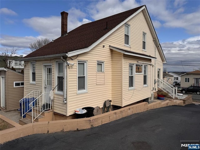 exterior space with entry steps, a shingled roof, and a chimney