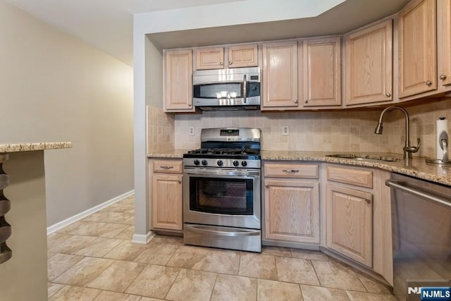 kitchen with a sink, light stone counters, backsplash, stainless steel appliances, and baseboards