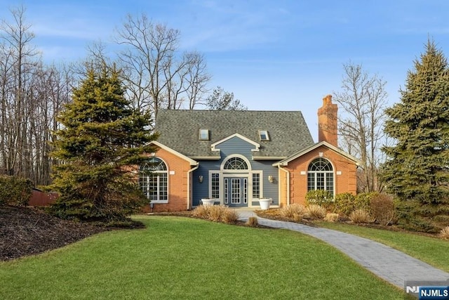 view of front of home featuring driveway, roof with shingles, a chimney, a front lawn, and brick siding