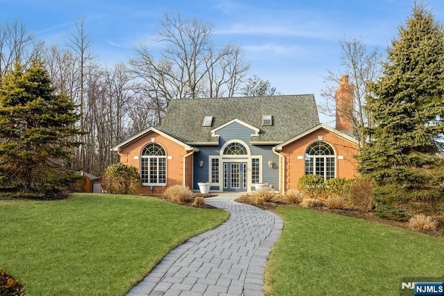 view of front of property with a front yard, roof with shingles, a chimney, french doors, and brick siding