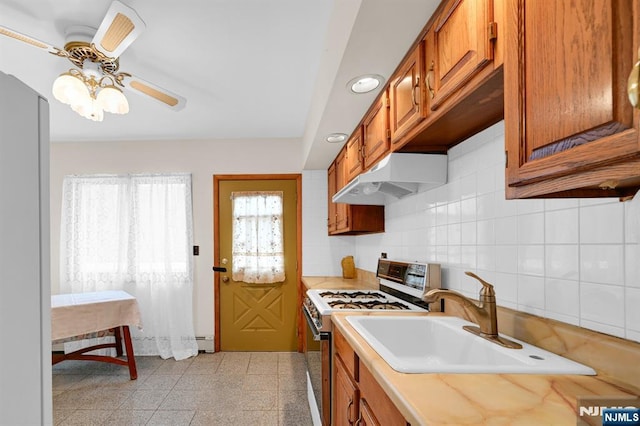 kitchen with brown cabinetry, a sink, under cabinet range hood, and gas range oven