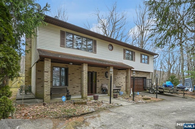 multi unit property with a garage, covered porch, aphalt driveway, and brick siding