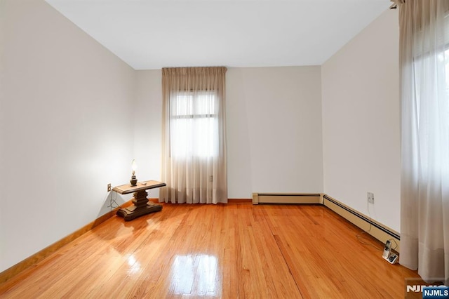 spare room with a baseboard heating unit, light wood-style flooring, and baseboards