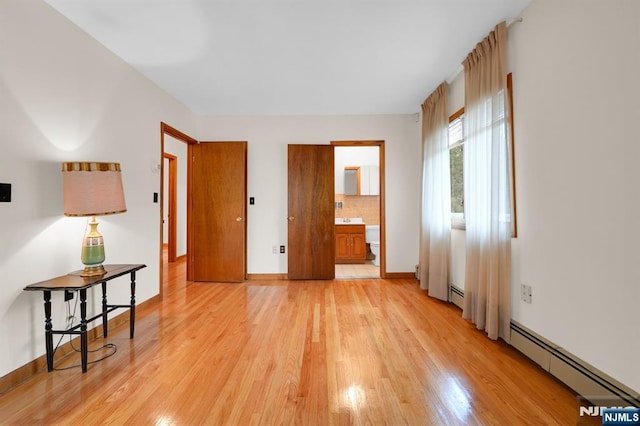 empty room featuring light wood-style flooring, a baseboard heating unit, and baseboards