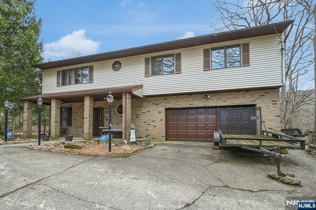 view of front of house featuring an attached garage, driveway, brick siding, and a porch