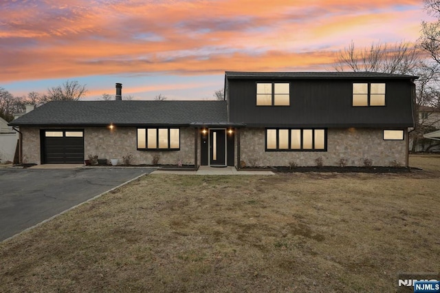 view of front of home with stone siding, driveway, an attached garage, and a lawn