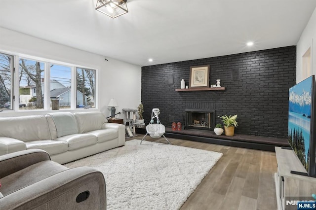 living room with recessed lighting, a fireplace, brick wall, and wood finished floors