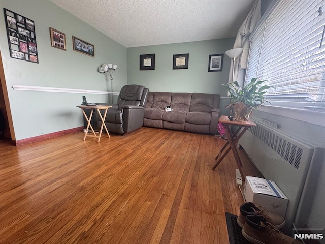 living area with radiator heating unit, baseboards, a textured ceiling, and hardwood / wood-style floors