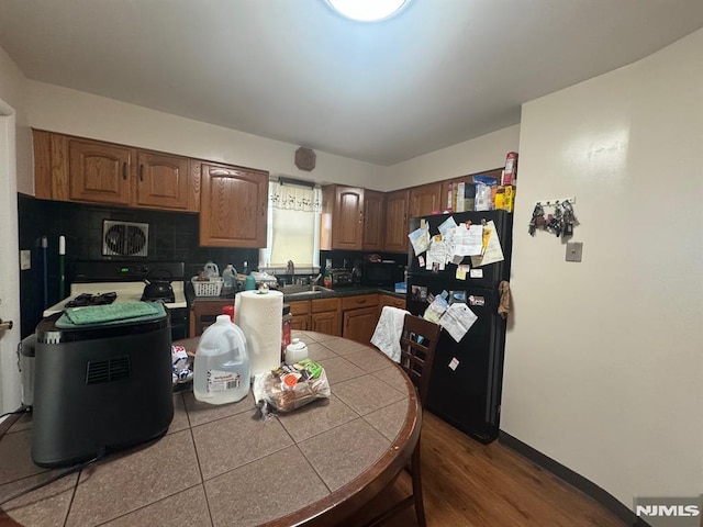 kitchen with a sink, backsplash, tile counters, freestanding refrigerator, and brown cabinets