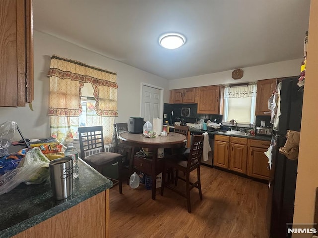 kitchen with dark wood-style floors, brown cabinetry, freestanding refrigerator, a sink, and dishwashing machine