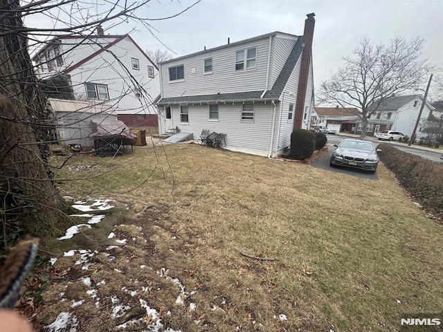 rear view of house featuring a chimney and a lawn