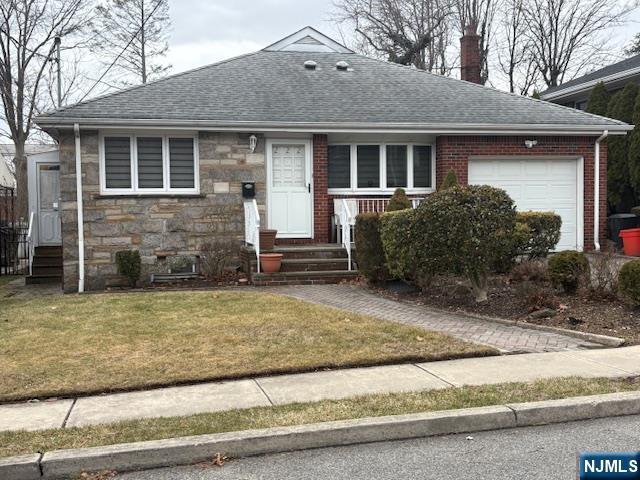 view of front of house with roof with shingles, a chimney, a garage, stone siding, and a front lawn