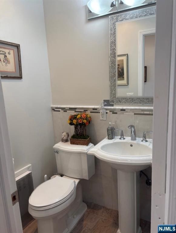 half bathroom with wainscoting, a sink, tile walls, and toilet