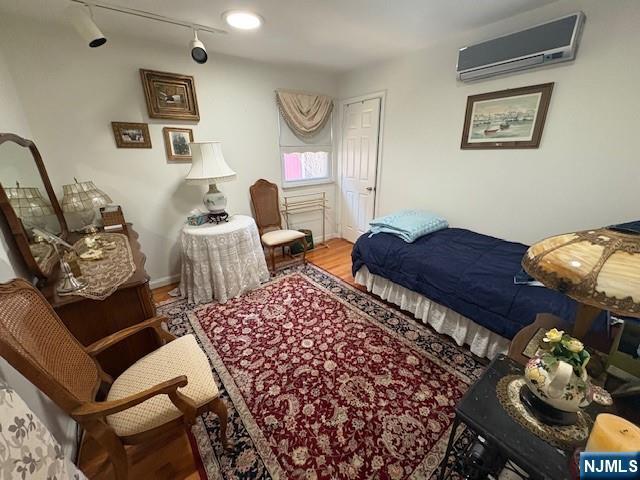 bedroom with a wall mounted air conditioner, wood finished floors, rail lighting, and baseboards