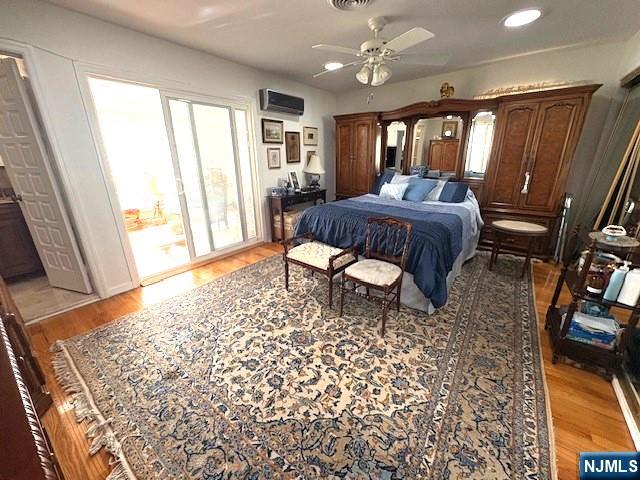 bedroom with an AC wall unit, multiple windows, and light wood finished floors