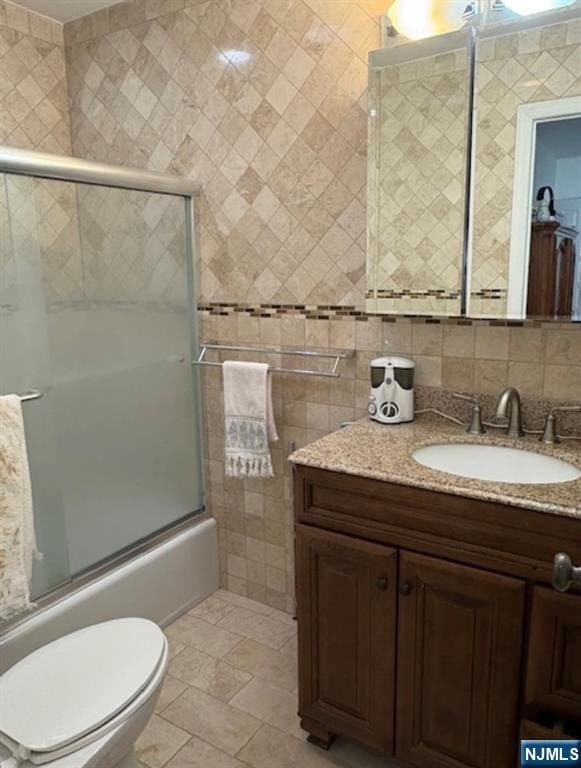 full bathroom with enclosed tub / shower combo, toilet, vanity, and tile walls