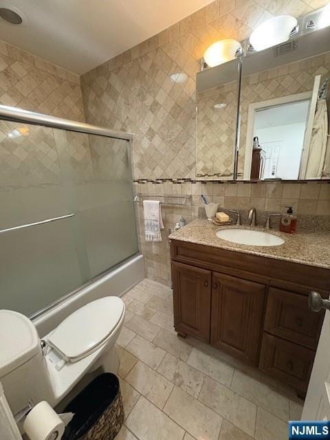 bathroom with enclosed tub / shower combo, tile walls, toilet, and vanity