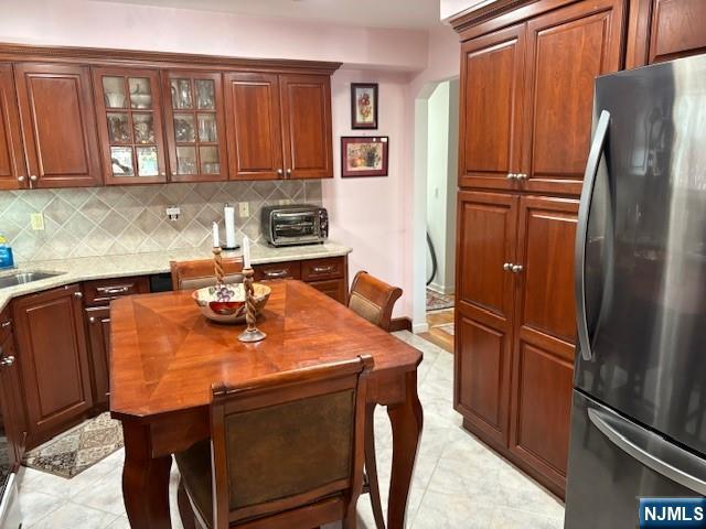 kitchen with arched walkways, a sink, freestanding refrigerator, decorative backsplash, and glass insert cabinets