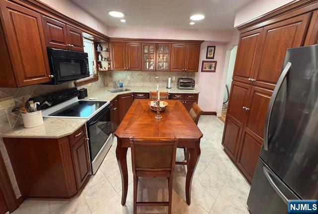 kitchen featuring electric stove, decorative backsplash, freestanding refrigerator, a sink, and black microwave