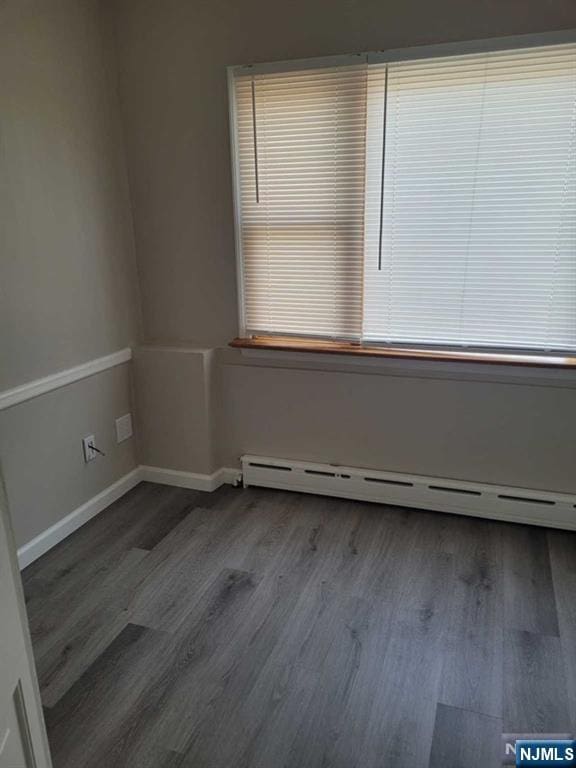 spare room with a baseboard heating unit, baseboards, and wood finished floors