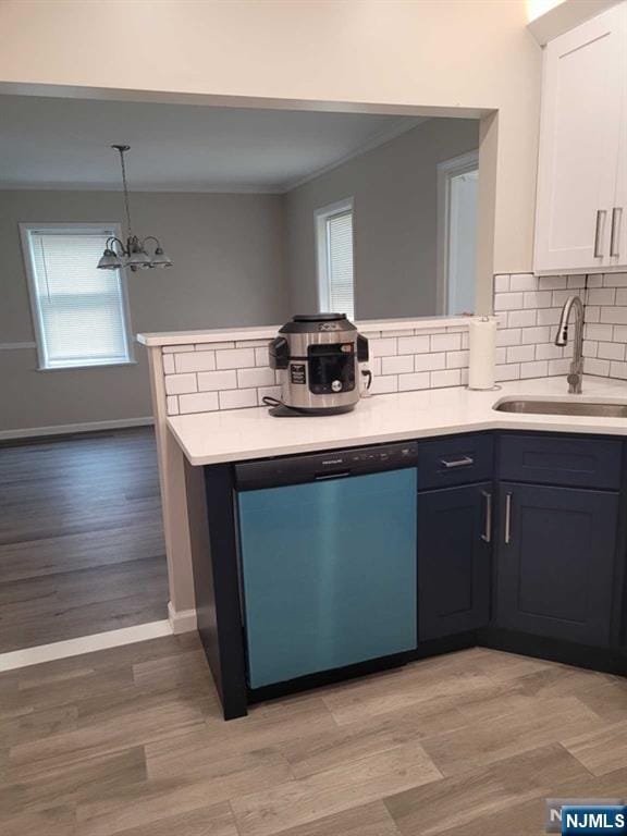 kitchen featuring dishwashing machine, a peninsula, light countertops, white cabinetry, and a sink