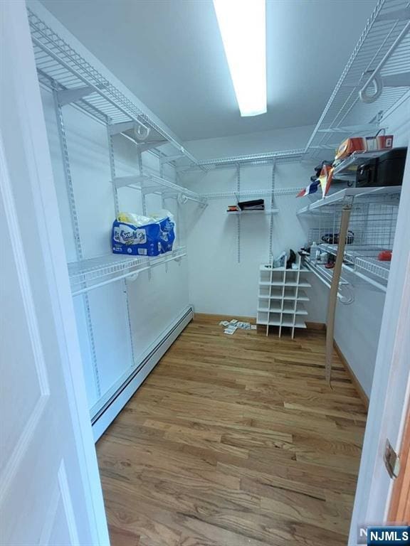 spacious closet with a baseboard heating unit and wood finished floors