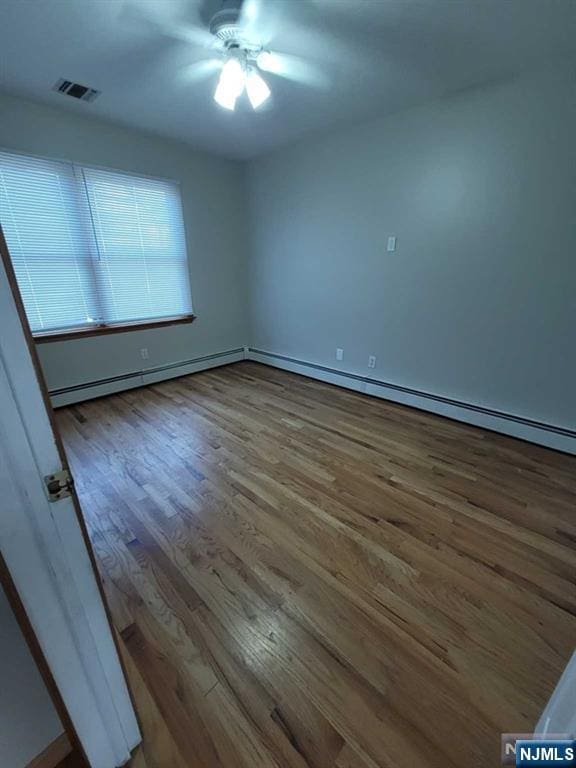 empty room featuring a ceiling fan, a baseboard radiator, visible vents, and wood finished floors