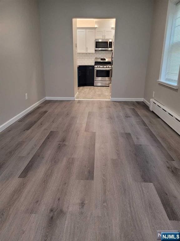 unfurnished living room featuring baseboard heating, wood finished floors, and baseboards