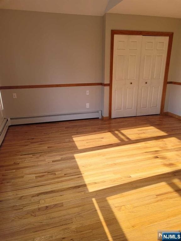 unfurnished bedroom featuring a baseboard heating unit, a closet, wood finished floors, and baseboards