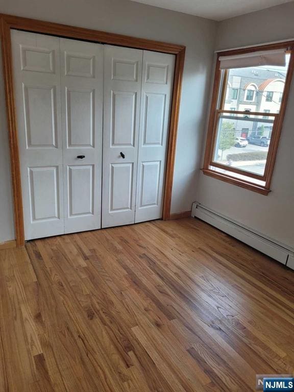 unfurnished bedroom featuring baseboard heating, a closet, light wood-type flooring, and baseboards