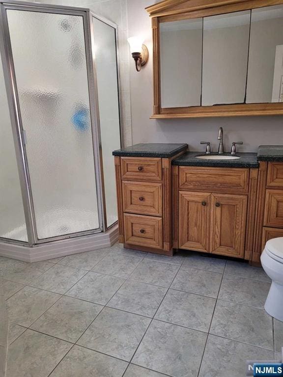 bathroom featuring toilet, a shower stall, vanity, and tile patterned floors