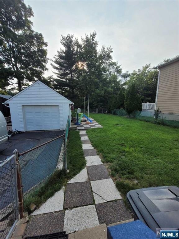 view of yard featuring a garage, driveway, an outdoor structure, and fence