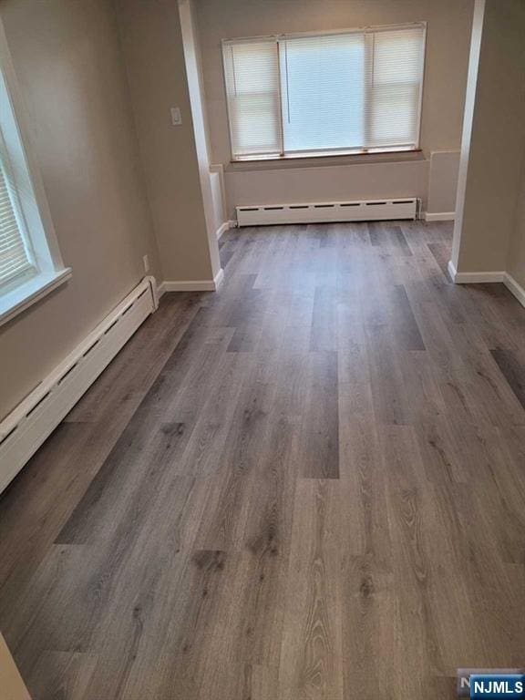 interior space with a baseboard heating unit, wood finished floors, and baseboards